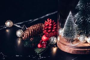 Weihnachtsbaum und leuchtende Lichterkette und Tannenzapfen und Misteldekoration auf Marmortisch foto