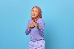 Porträt einer fröhlichen jungen asiatischen Frau, die mit dem Finger auf die Kamera auf blauem Hintergrund zeigt