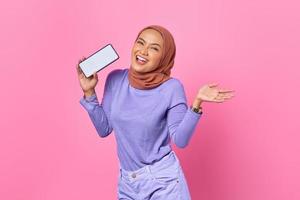 Porträt einer fröhlichen jungen asiatischen Frau, die Handy-Bildschirm auf rosafarbenem Hintergrund zeigt