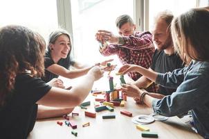 eine Gruppe kreativer Freunde, die auf einem Holztisch sitzen. Die Leute hatten Spaß beim Spielen eines Brettspiels. foto