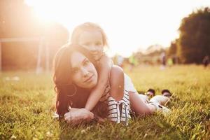 glückliche mutter und tochter, die sich in einem park in der sonne auf einem hellen sommerhintergrund aus kräutern umarmen. foto