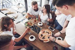 leckere Pizza auf dem Tisch, mit einer Gruppe junger lächelnder Leute, die sich im Pub ausruhen? foto