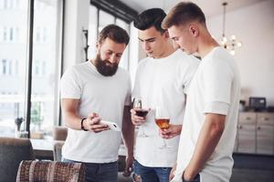 Fröhliche alte Freunde kommunizieren miteinander und telefonieren, mit Gläsern Whisky oder Wein in der Kneipe. Konzept der Unterhaltung und des Lebensstils. Wifi-verbundene Leute in Stehtischtreffen foto