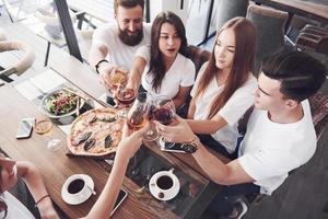 Freunde trafen sich am Tisch bei leckerem Essen mit Gläsern Rotwein, um einen besonderen Anlass zu feiern foto