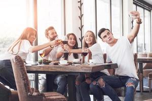 Eine Gruppe von Menschen macht in einem Café ein Selfie-Foto. die besten Freunde versammelten sich an einem Esstisch, aßen Pizza und sangen verschiedene Getränke foto