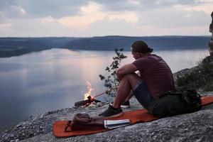 erfolgreicher Mann Wanderer auf Felsen mit Lagerfeuer. Reisen entlang von Bergen und Küste, Freiheit und aktives Lifestyle-Konzept foto