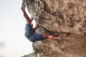 Ein junger Mann Kletterer klettert auf einen Felsen. extreme Ruhe, Lebensstil frei und im Geist starke Menschen foto