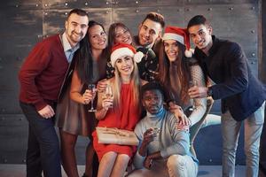 das neue Jahr kommt. Gruppe fröhlicher junger multiethnischer Menschen in Weihnachtsmützen auf der Party, die ein emotionales Lifestyle-Menschenkonzept aufwerfen foto