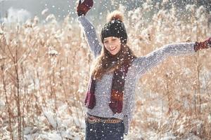 Schönheit Wintermädchen bläst Schnee im frostigen Winterpark. draußen. fliegende Schneeflocken. sonniger Tag. hinterleuchtet. fröhliche Schönheit junge Frau, die Spaß im Winterpark hat foto