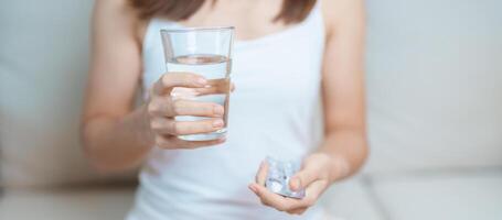 Frau Hand halten Medizin Schmerzmittel Pille und Wasser Glas auf das Sofa beim heim, nehmen zum Kopfschmerzen, Bauch schmerzen, Durchfall Schmerzen von Essen Vergiftung, Endometriose, Hysterektomie und Menstruation- foto