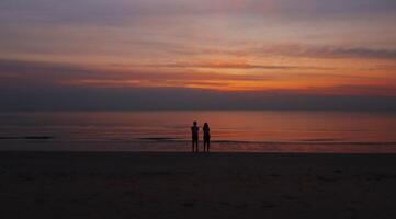 Silhouette von das Paar Stehen beim das Strand suchen Sonnenaufgang beim das Strand von Thailand foto