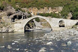 ein Person Kreuze das kadiut Brücke im Benje, Erlaubnis, Albanien. Stein Brücke Über das Fluss. foto