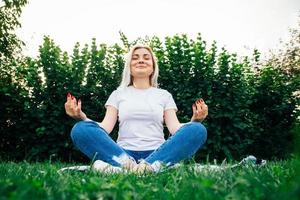 Frau mit Kopfhörern sitzt in meditativer Pose auf grünem Gras foto