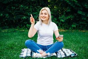 Frau mit Kopfhörern und Smartphone in den Händen auf grünem Gras foto