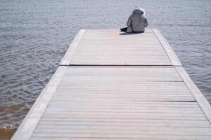 ein Mann ist Sitzung auf ein hölzern Seebrücke und suchen beim das See. foto