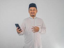 Moslem asiatisch Mann lächelnd glücklich während halten Handy, Mobiltelefon Telefon foto