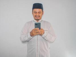 Moslem asiatisch Mann lächelnd glücklich wann SMS mit seine Handy, Mobiltelefon Telefon foto