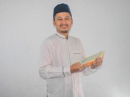 Moslem asiatisch Mann lächelnd beim das Kamera während halten ein al-Qur'an foto
