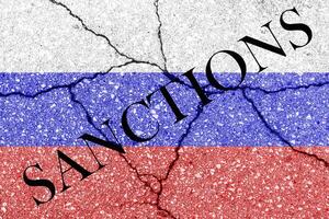 das Flagge von das Russisch Föderation auf ein geknackt Beton Mauer mit das Wörter Sanktionen. Konzept foto