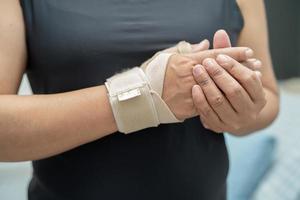 asiatische frauen mittleren alters verwenden elastische bandage zur behandlung des de quervain-syndroms an hand und finger im büro. foto