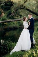 Der Bräutigam und die Braut gehen im Wald in der Nähe eines schmalen Flusses spazieren foto