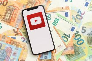 Kiew, Ukraine - - April 1, 2024 Youtube Symbol auf Smartphone Bildschirm auf viele Euro Geld Rechnungen foto