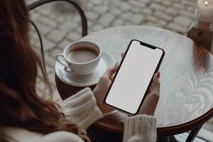 Hände halten Telefon mit Weiß Attrappe, Lehrmodell, Simulation Bildschirm gegen Kaffee Tabelle Hintergrund foto