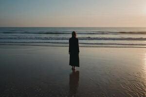 eine Frau, die am Strand bei Sonnenuntergang steht foto