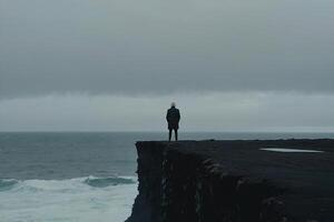 ein Mann Stehen auf das Kante von ein Cliff mit Blick auf das Ozean foto