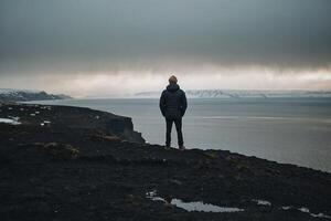 Mann Stehen auf das Kante von das Cliff suchen beim das Ozean foto