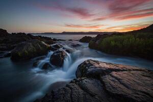 ai generiert ein schön Sonnenuntergang Über das Ozean mit Felsen und Wasser foto