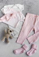 einstellen von Baby Bodys, Hose, Socken und gestrickt Spielzeug auf grau Hintergrund. foto