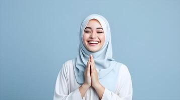 Süd-Ost asiatisch Frau tragen Schal ist beten und lächelnd auf Blau Hintergrund foto