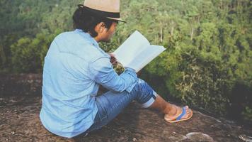asiatische Mannreisen entspannen sich im Urlaub. Sitze entspannen, Bücher lesen auf felsigen Klippen. auf dem Berg. in Thailand foto