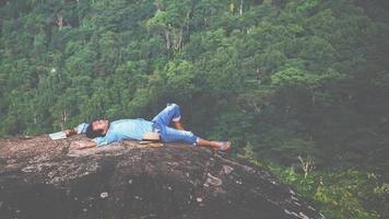 asiatische Mannreisen entspannen sich im Urlaub. schlafen entspannen lesen bücher auf felsigen klippen. auf dem Berg. in Thailand foto