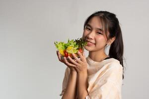 Porträt von ein glücklich spielerisch asiatisch Mädchen Essen frisch Salat von ein Glas Schüssel nach trainieren beim heim. jung Dame genießen gesund Ernährung und organisch Essen, haben Vegetarier Mahlzeit foto