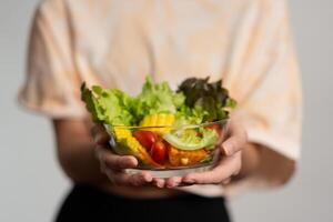 Porträt von ein glücklich spielerisch asiatisch Mädchen Essen frisch Salat von ein Glas Schüssel nach trainieren beim heim. jung Dame genießen gesund Ernährung und organisch Essen, haben Vegetarier Mahlzeit foto