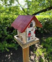 ein handgemalt Vogelhaus mit ein beschwingt rot Dach und Abbildungen von Vögel, thront draußen mit ein üppig Grün Hintergrund foto