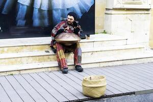 Baku, Aserbaidschan - - Dezember 02, 2023 . ein jung Kerl mit Dreadlocks und ein Bart Theaterstücke ein Schlagzeug Musical Instrument hängen im das Stadt auf das Straße. foto