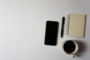 Kaffee, Clever Telefon, Notizbuch und Stift auf Weiß Hintergrund. foto