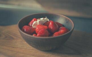 Zuhause Küche. Erdbeeren mit Sahne im ein Lehm Teller auf ein hölzern Tafel foto