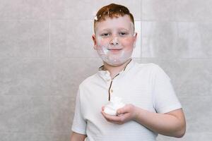 komisch Junge im das Bad mit Rasieren Sahne auf seine Gesicht foto