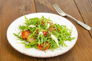 Gericht aus Rucola, Tomaten, Trockenfleisch und Käse. Salat auf Teller auf Holzuntergrund