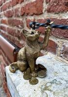 ein künstlerisch Bronze- Katze Figur halten ein Paar von Brille, umgeben durch verstreut Münzen auf ein Stein Leiste. foto