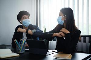 Geschäft oder Buchhalter tragen Maske und stoßen Ellbogen zum behalten Sozial Entfernung stattdessen von Umarmungen oder Handschlag beim Morgen im Zuhause Büro. foto