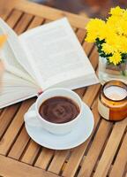 Gelb Blumen, Tasse von heiß trinken und Buch auf hölzern Tabelle draussen. Herbst immer noch Leben foto