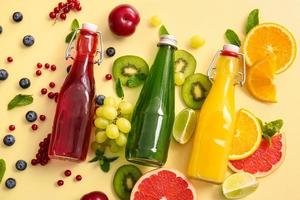 Flaschen mit gesundem Saft und Früchten auf farbigem Hintergrund foto
