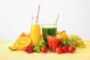 Gläser mit gesundem Saft, Obst und Gemüse auf hellem Hintergrund foto