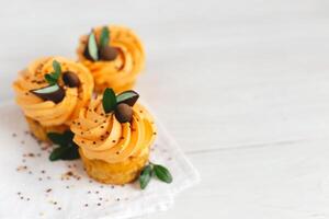 lecker Kürbis Cupcakes mit Orange Sahne und Dekoration auf Weiß hölzern Tisch. foto