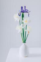 Strauß von zärtlich Narzisse Narzisse und Iris Blumen im ein Vase auf ein Weiß Tisch. foto